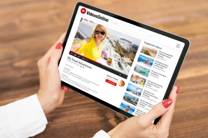 Une personne tient une tablette affichant une vidéo YouTube de voyage pour illustrer un outil de résumé.
