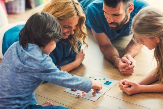 Une famille joyeuse partage un moment convivial autour de jeux de société sur le sol du salon.