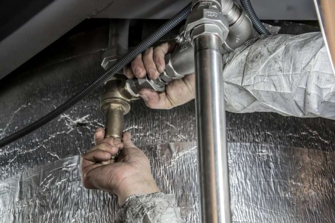 Un technicien répare des tuyaux dissimulés dans une installation technique.