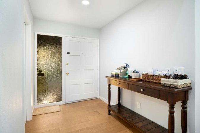 Une table console en bois sombre ornée d'objets de décoration est placée dans une entrée lumineuse à côté d'une porte blanche.